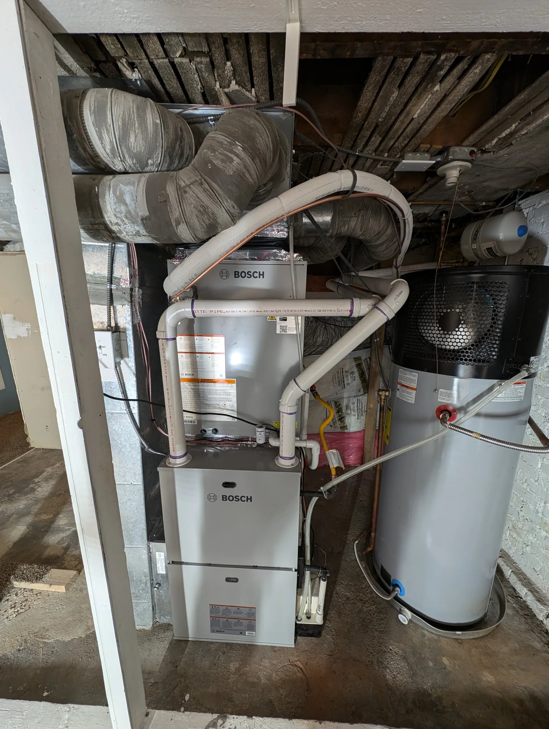 A heat pump water heater beside a Bosch furnace and air handler in a basement